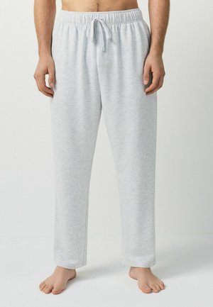 Man wearing light grey drawstring lounge pants, standing barefoot against a plain light background.