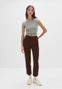 T-shirt verde deschis, croială ajustată, blugi închiși la culoare cu talie înaltă, adidași crem și șosete albe. Design simplu, cu o croială scurtă și picior drept.