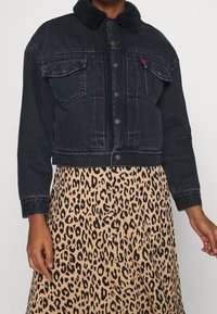 Mörk denimkort jacka med svart pälskrage, med knappstängning och två bröstfickor, bärs över en leopardmönstrad kjol.