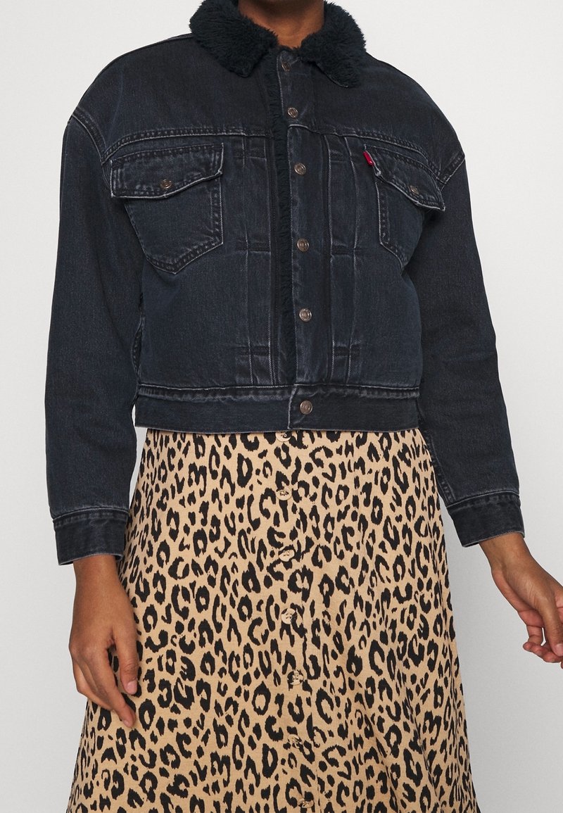 Mörk denimkort jacka med svart pälskrage, med knappstängning och två bröstfickor, bärs över en leopardmönstrad kjol.