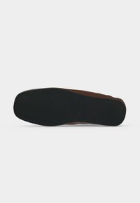 Chaussure marron couchée sur le côté montrant une semelle noire, plate et texturée avec un bout carré arrondi et un léger talon.