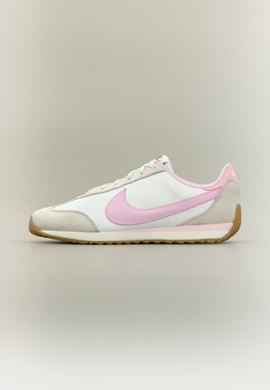 Baskets blanches et beiges avec un logo Nike rose en forme de virgule et un accent sur le talon, semelle marron clair, présentées de profil sur un fond neutre.