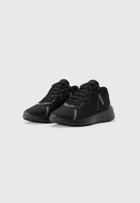 Un par de zapatillas deportivas negras de corte bajo con suelas texturizadas y detalles reflectantes sobre un fondo blanco.