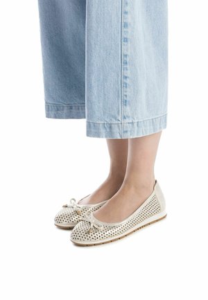 Bailarinas blancas perforadas con puntera redondeada y detalle de lazo, combinadas con pantalones de mezclilla de pierna ancha en tono azul claro, cortados a la altura del tobillo.