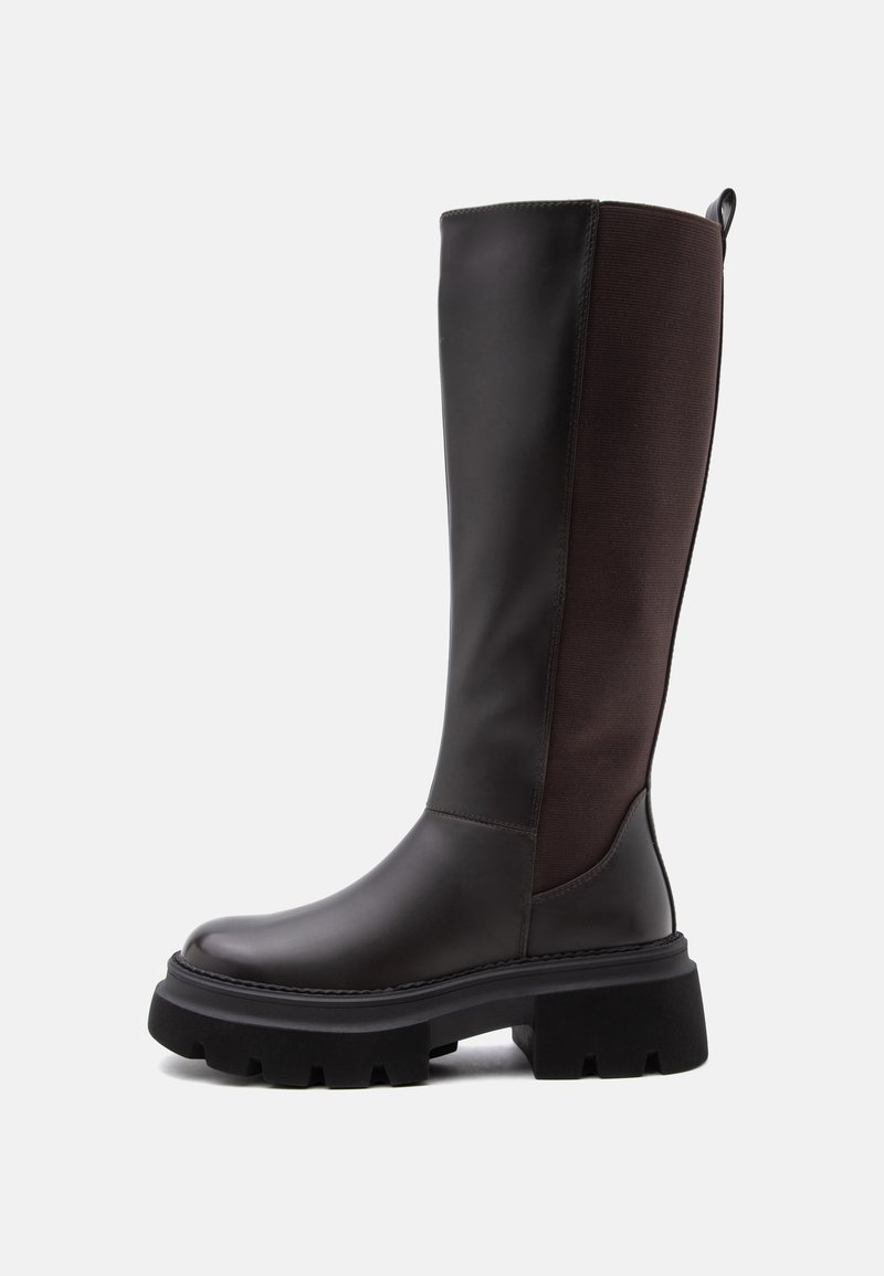 Botte noire montante jusqu'au genou avec semelle épaisse crantée et panneau en tissu élastique à l'arrière, vue de profil sur un fond uni.