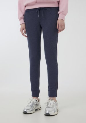 Pantaloni della tuta navy con vita elasticizzata, vestibilità affusolata e orli cinturino. Il materiale è morbido, con una leggera lucentezza e dettagli con cordoncino.