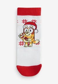 Chaussettes tricotées rouges et blanches avec un chien de dessin animé portant un chapeau de Noël et tenant un cadeau, avec des motifs de flocons de neige sur le fond blanc.