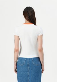 White short-sleeve top with an orange neckline, paired with a blue denim skirt featuring back pockets and a straight cut.
