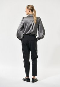 Graue Satinbluse mit ballonärmel, kombiniert mit schwarzen Hosen und schwarzen Schuhen. Die Bluse hat einen strukturierten Kragen und eine glatte Textur.