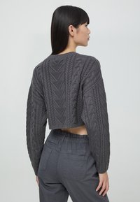 Maglione grigio cropped con design a treccia testurizzata, scollo rotondo e maniche lunghe. Abbinato a pantaloni grigi a vita alta.