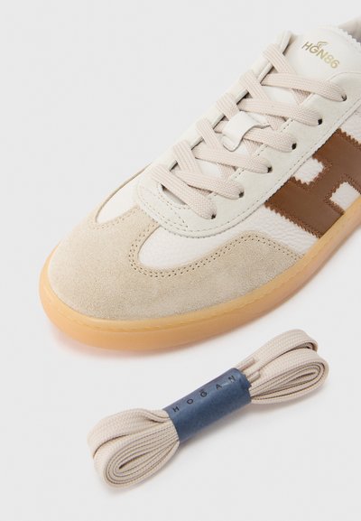 Λευκό και μπεζ αθλητικό παπούτσι με υφές σουέτ και δέρματος, με καφέ λογότυπο, μπεζ κορδόνια και σόλα από καουτσούκ. Περιλαμβάνονται επιπλέον κορδόνια.