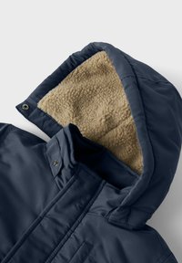 Giacca con cappuccio blu navy, dotata di un morbido rivestimento interno in pile beige, esterno liscio e chiusure a bottoni a pressione.