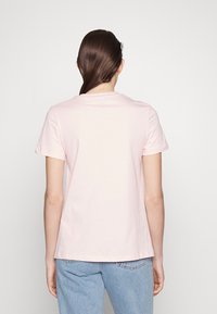Camiseta de algodón rosa claro con mangas cortas, cuello redondo y corte recto, mostrada desde la parte trasera sobre un fondo liso.