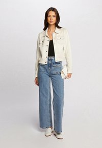 Lichtgrijze suède cropped jack met twee borstzakken, gecombineerd met hooglopende blauwe denim wijde pijpen jeans en witte instappers.