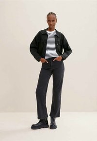 Črna denim jakna preko bele in črne črtaste majice, v kombinaciji s temnimi hlačami in črnimi gležnjarji. Preprost dizajn, priložnostna kroja.