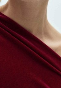 Tissu en velours bordeaux drapé élégamment avec une texture douce et un éclat naturel ; surface lisse avec des plis subtils mettant en valeur sa forme.