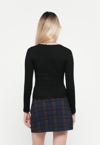 Haut noir à manches longues avec une bordure en dentelle au niveau de l'encolure, associé à une jupe à carreaux aux couleurs bleue, brune et grise. Texture lisse.