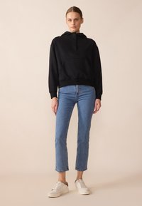 Felpa nera con cappuccio e tasca a marsupio, abbinata a jeans azzurri a gamba dritta e sneakers bianche. Texture liscia, design casual.