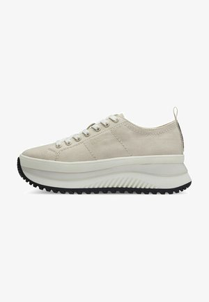 Zapatilla de lona beige con cordones blancos, suela de plataforma blanca gruesa, banda de goma negra, detalles texturizados y una tira en el talón.