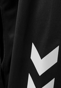 Schwarzer Stoff mit einem auffälligen weißen Chevron-Muster. Die Textur wirkt glatt und das Design ist klar und modern.