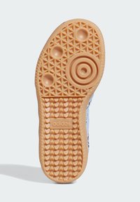 Gummisohle von Turnschuhen mit einem strukturierten Muster aus kreisförmigen und rhombischen Formen. Überwiegend in Hellbraun mit einem prägten Markenlogo.