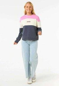 Felpa multicolore con strisce rosa, crema e blu navy. Tessuto morbido con polsini e orlo a costine, abbinata a jeans azzurri.