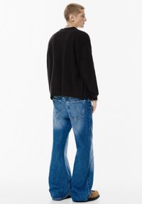 Przesadny czarny sweatshirt z długimi rękawami, w połączeniu z jasnoniebieskimi dżinsami w kształcie dzwonów z tylnymi kieszeniami i wyblakłą fakturą. Brązowe obuwie.