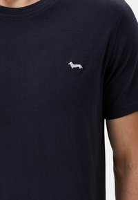 T-shirt blu navy a maniche corte, con un piccolo design ricamato di un bassotto bianco nella zona sinistra del petto. Tessuto morbido.