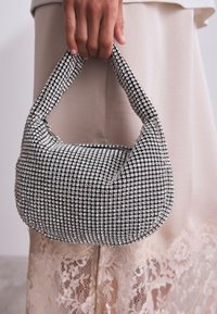Silver rhinestone-embellished bag with a rounded shape and a short, padded handle. The base features a smooth texture and intricate patterns.