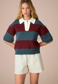 Sweter dzianinowy w burgundowe i tealowe paski, krótki rękaw oraz biały kołnierzyk. W zestawie z kremowymi szortami w pionowe prążki.