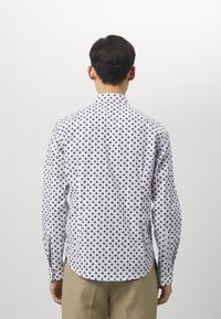 Witte shirt met marineblauw palmentakkenpatroon, lange mouwen, klassieke kraag, rechte zoom en een gladde textuur. Draag met beige broeken.