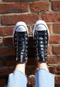 Sorte høye sneakers med hvit gummitåhette, svarte snører og glatt lær overdel, kombinert med slitt lys blå dongeribukse.