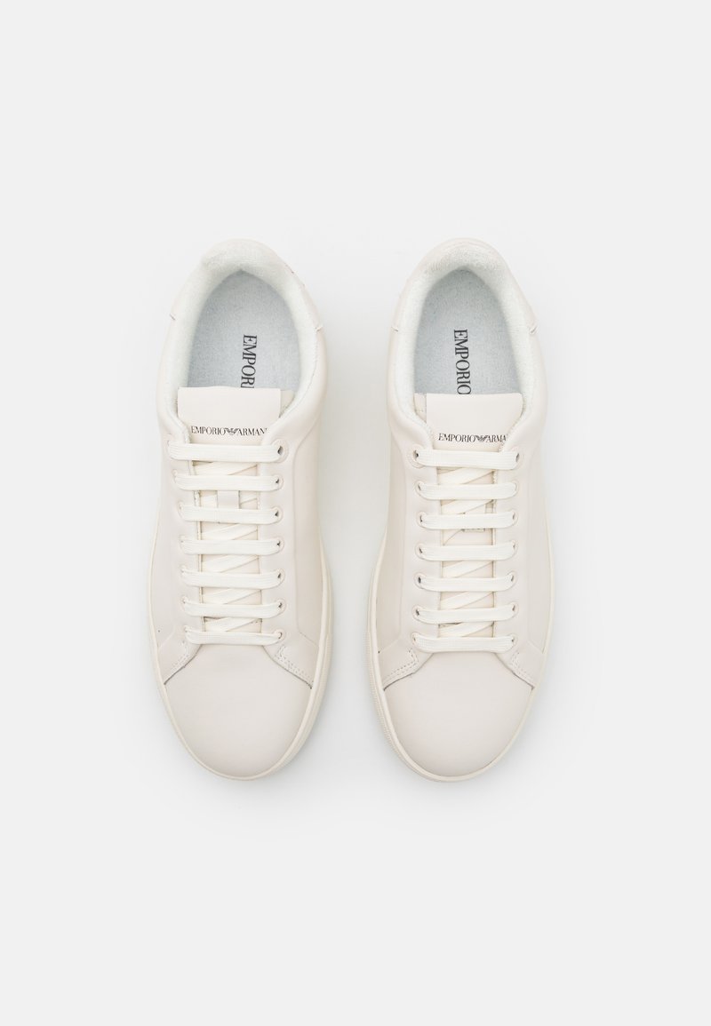 Baskets en cuir blanc avec bout rond, lacets plats et logo sur la languette. Doublure douce et semelle texturée visibles. Design minimaliste.