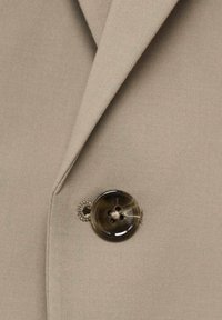 Beige blazer fabric with a smooth texture, featuring a large, dark button with a glossy finish, and subtle stitching detail around the buttonhole.