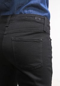 Sorte denim jeans med en tettsittende design, med standard baklommer og kontrasterende sømdetaljer. Stoffet har en jevn tekstur.