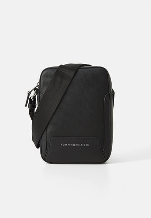 Zwarte rechthoekige crossbodytas met verstelbare riem, gestructureerde voorkant en "Tommy Hilfiger"-logo op het voorvak.
