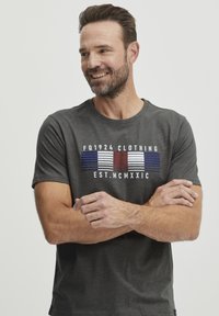 Grå bomull T-skjorte med brystgrafikk i blå, rød og hvit stripe samt teksten "FQ1924 CLOTHING EST. MCMXXIC." Korte ermer.