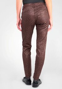 Pantalons imprimés léopard marron avec une coupe slim, présentant une texture lisse et des poches arrière, associés à des chaussures noires brillantes.
