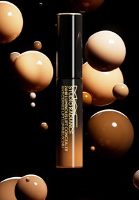 Il correttore MAC Studio Radiance 24H Luminous Lift in un tubo nero lucido con accenti dorati, presenta un prodotto beige-marrone su uno sfondo nero.