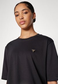 T-shirt nero a maniche corte in tessuto leggero con un patch logo triangolare sul lato sinistro del petto. Texture liscia e vestibilità comoda.