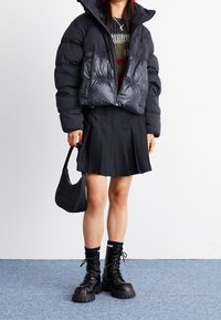 Svart puffjacka med dragkedja framtill, i kombination med en svart veckad kjol. Svarta snörstövlar med kraftiga sulor och en texturerad svart axelväska.