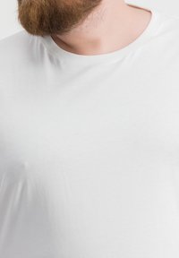 Maglietta in cotone bianco con scollatura rotonda, maniche corte e una texture liscia e uniforme, parzialmente visibile sopra l'area del petto.