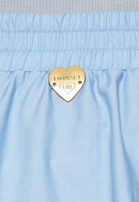 Ljusblått tyg med en strukturerad yta, med en elastisk midja och en gyllene hjärtformad metalltag som är graverad med "TWINSET."