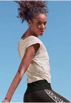 Beiges Kurzarmhemd mit lockerem Schnitt, kombiniert mit schwarzen, hoch taillierten Leggings mit einem Leopardenmusterstreifen an der Seite.