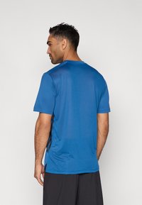 Μπλε αθλητική μπλούζα από ύφασμα που απομακρύνει την υγρασία. Κοντά μανίκια, στρογγυλή λαιμόκοψη, με διακριτικές λεπτομέρειες στα πλάγια και απαλό ύφασμα.