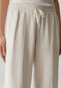 Lichtbeige broeken van textuurstof, met een elastische tailleband en een trekkoord, voorzien van zijplooien en een relaxte pasvorm.