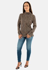 Top de leopardo con cuello estilo cowl en tejido suave, mangas largas, combinado con jeans skinny de mezclilla azul claro y sandalias de tacón negro.