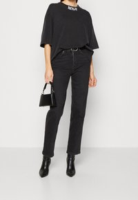Camiseta negra de gran tamaño con el logo blanco "REPLAY", combinada con jeans negros de pierna recta y botas negras de tacón puntiagudo. Pequeño bolso negro.