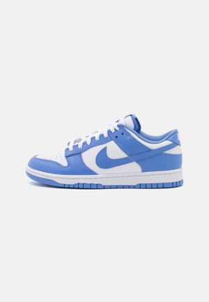 Niedriger Sneaker in Weiß und Hellblau mit Nike-Swoosh, weißen Schnürsenkeln und perforierter Zehenbox auf einfachem hellem Hintergrund.