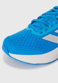 Lengvas bėgimo batelis su kvėpuojančiu mėlynu tinklinio viršumi, sustiprintu piršto apsaugos dangteliu ir baltu paminkštintu padu. Turi mėlynas raištelius ir metalinius akcentus.